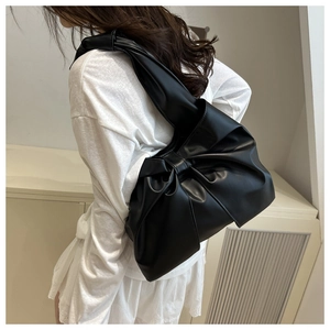 Side view of model wearing black oversized bow shoulder bag with glossy PU leather texture