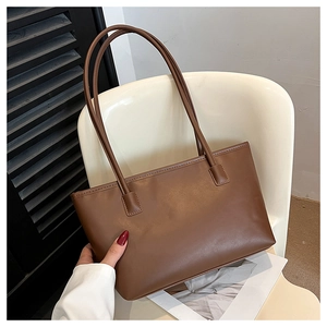 Detail view of large brown faux leather tote bag with slim shoulder straps on white chair