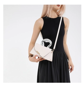 Detail view of heart-shaped silver metal handle on a cream white crossbody bag