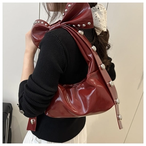 Detail showing oversized bow design and silver stud rivets on the dark red shoulder bag