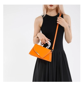 Close-up of bright orange crossbody bag with bold silver U-shaped metal handle and strap