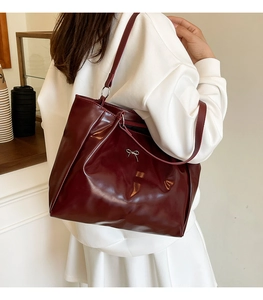 Detail of dark red glossy shoulder bag featuring a silver metal bow charm ornament
