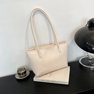 Minimalist beige tote bag with slim shoulder straps on a stylish desktop setting
