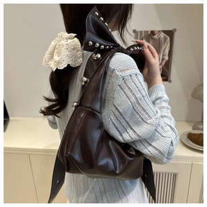 Dettaglio di una borsa a spalla in pelle marrone lucida con borchie argentate