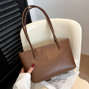 Large brown leather tote bag with long handles placed on a chair in a minimalist setting