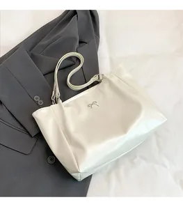 Detail of cream white leather tote bag with silver bow accent on dark grey suit jacket
