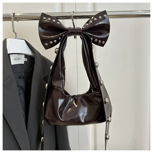 Dettaglio borsa in pelle verniciata marrone scuro con rivetti e fiocco decorativo