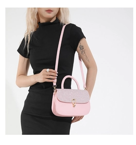 Detail of pink crossbody bag with glitter flap, round handle and gold metal clasp on model