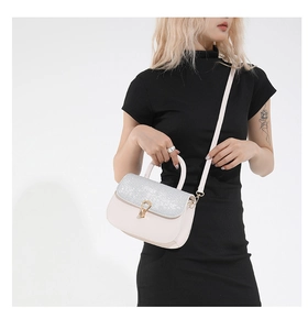 Detail of a minimalist square crossbody bag featuring a silver glitter flap and gold hardware