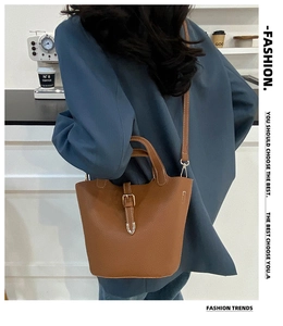 Brown lychee-grain bucket bag with belt buckle shown as a crossbody on a model