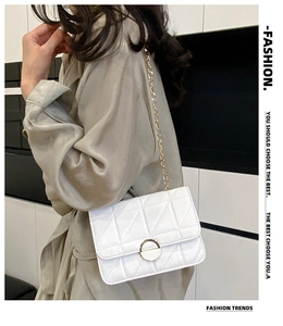 Detail of white quilted crossbody bag with gold chain strap worn by a model in a beige coat