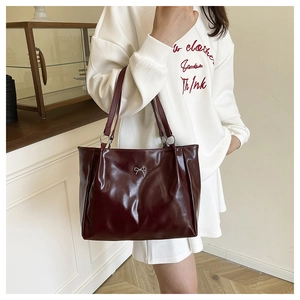 Detail of burgundy glossy leather tote bag with elegant silver bow metal hardware decoration
