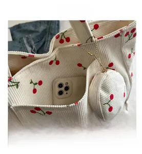 Close-up of corduroy tote bag featuring cherry prints with mini pouch and phone pocket