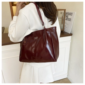 Close-up of glossy burgundy leather tote bag featuring a silver metal bow pendant detail
