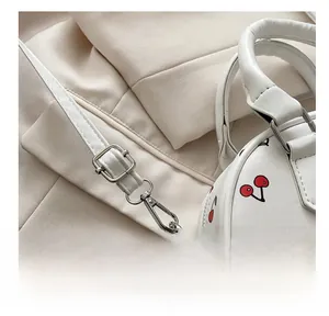 Close-up of adjustable silver metal buckle and red cherry print on white leather bag