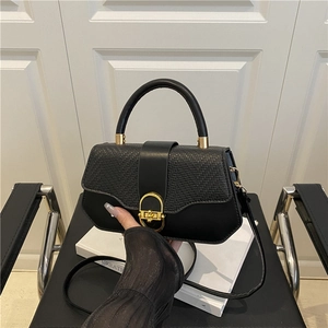 Black leather handbag with woven flap and gold circular clasp on a white background
