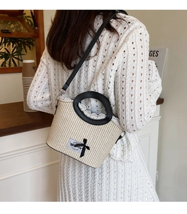 Détail d'un sac en paille avec bordure en dentelle blanche et noeud noir sur la bandoulière