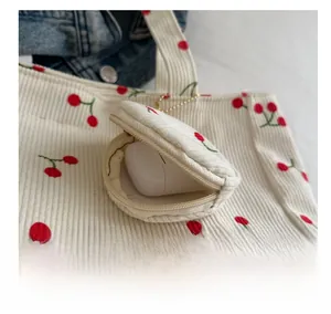 Macro detail of cream corduroy cherry charm bag showing zipper and wireless earphones inside