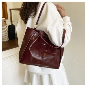 Detail of burgundy tote bag featuring a shiny finish and silver bow accent in daily use