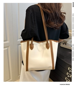 Detail of a large beige leather tote bag with brown straps worn on a woman's shoulder