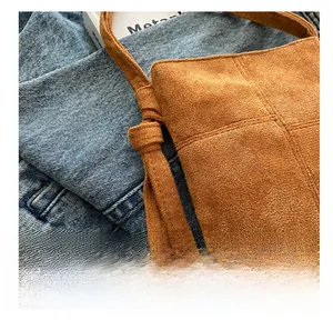 Detail of brown suede mini crossbody bag with knotted strap on denim fabric
