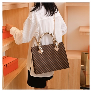 Detail of a large monogram tote bag with decorative silk scarf on the handle and strap