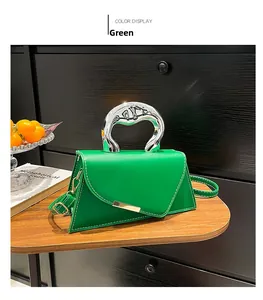 Detail of green crossbody bag with silver curved handle and contrast stitching on wood