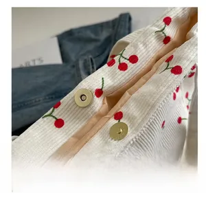 Detail of cherry embroidery on white corduroy bag with golden magnetic snap button