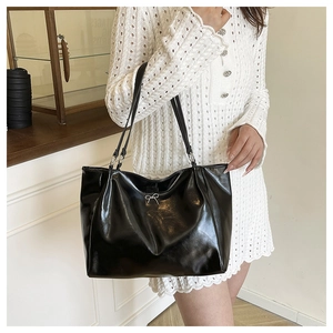 Detail of glossy black PU tote bag featuring a silver metal bow and pleated side texture
