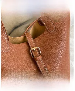 Macro detail of brown lychee leather handbag featuring gold buckle and contrast stitching