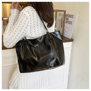 Close-up of a glossy black tote bag with a silver bow accent worn by a model in a dress