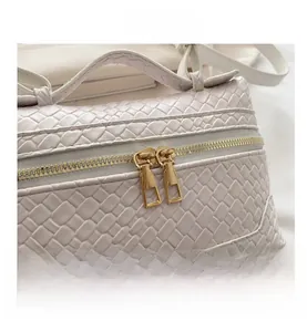 Detail of cream woven handbag with luxury gold double zippers and textured leather