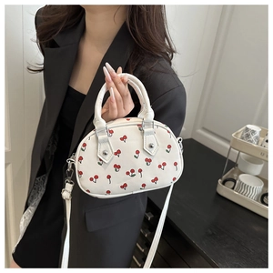 Close-up of white mini handbag with red cherry print and silver metallic buckle details
