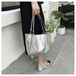 Detail of silver metallic tote bag featuring a delicate metal bow charm and trapezoid shape