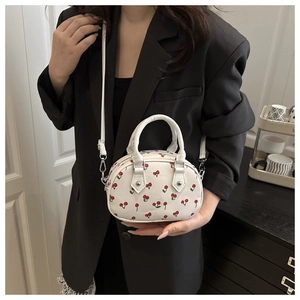 White mini Boston bag with red cherry print featuring top handles and long strap