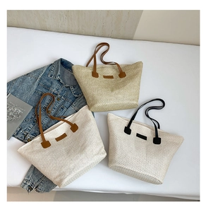 Flat lay of large straw tote bags in beige and white with leather straps and woven texture