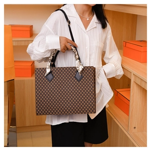 Detail of checkered shoulder bag with decorative silk scarf handle on model in boutique