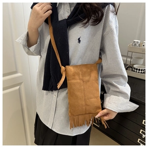 Detail of caramel suede crossbody bag with fringe tassels and patchwork on striped shirt