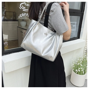 Detail of silver tote bag with metal bow and black wide textile shoulder strap