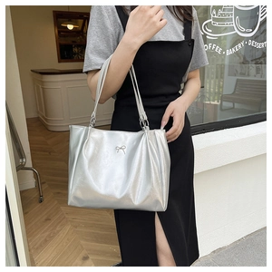 Detail of silver metallic tote bag with decorative bow shown in a casual outdoor setting