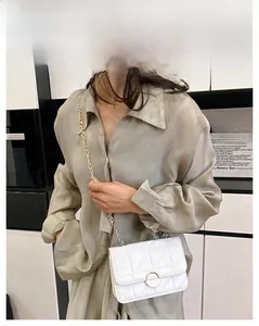 Close-up of white quilted crossbody bag with gold chain strap and metal ring buckle