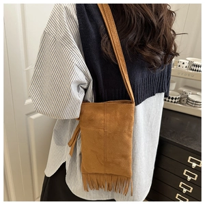 Detail of a brown suede crossbody bag with fringe accents and plaid stitching patterns