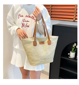 Detail of beige woven tote bag with premium brown leather handles and a textured finish
