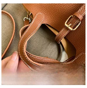 Close-up of brown lychee grain leather handbag featuring white stitching and gold buckle