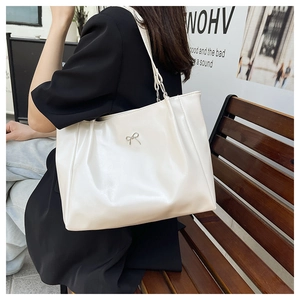 Detail of a beige tote bag with a silver metal bow and pleated faux leather design