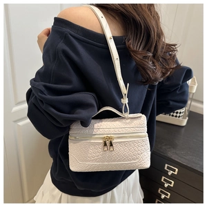 Detail of white woven leather box bag with gold double zippers and thin strap on a model