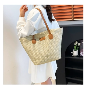 Detail of hand-woven straw tote bag with brown leather straps and fashion label
