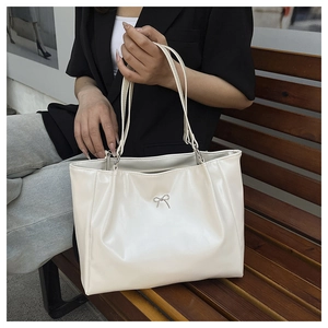 Close-up of creamy white PU leather tote bag featuring a silver metal bow and pleated details