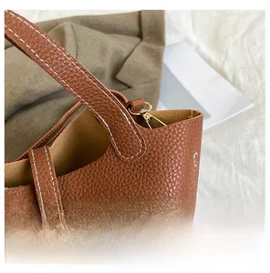 Close-up of litchi texture leather stitching and gold buckle on a brown tote bag