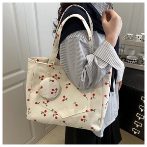 Détail du sac cabas en velours côtelé beige à motif cerises avec petite pochette sur un mannequin